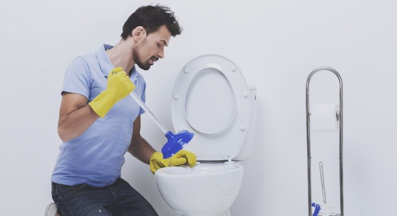 Man Wearing Gloves While Plunging the Toilet